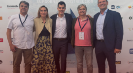 Five adults pose for a photo in front of a conference banner that reads 'Conocimiento, Visión, Futuro' with sponsor logos visible behind them.