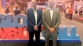 Two men in suits pose at a trade show booth with large colorful letters and the AFIBA logo in the background.