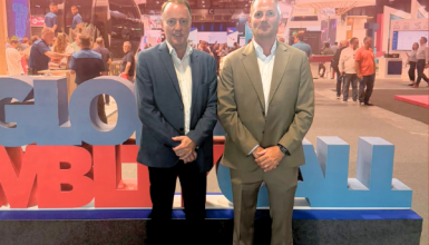 Two men in suits pose at a trade show booth with large colorful letters and the AFIBA logo in the background.