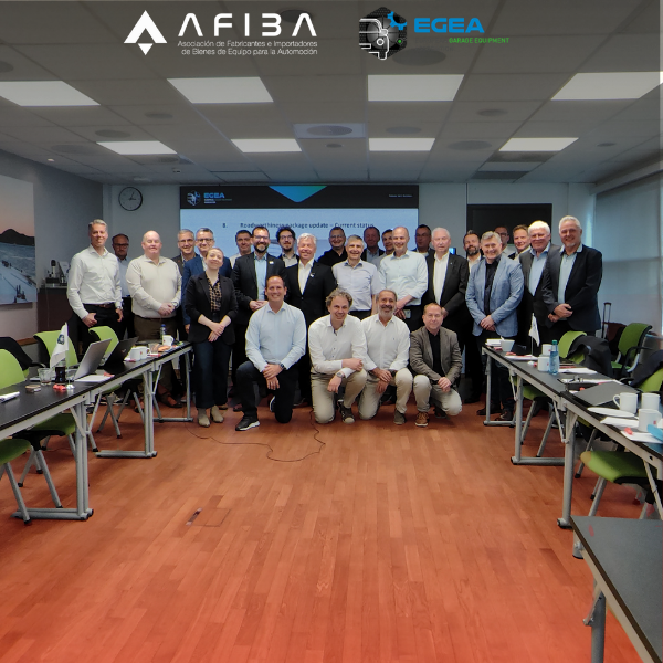 Group of about 30 professionals posing for a group photo in a seminar room, with a projector screen and logos behind them.