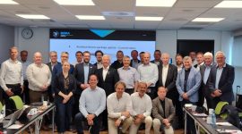 Group of business professionals posing for a photo in a conference room with a large screen behind them.