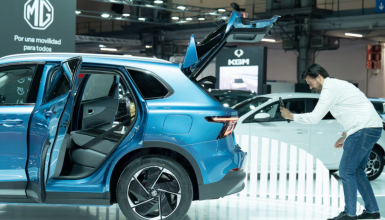 Man in a white shirt photographs a blue SUV on display with its doors and tailgate open at a car show.