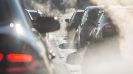 Line of cars in heavy traffic on a smoky, exhaust-filled road in daytime.