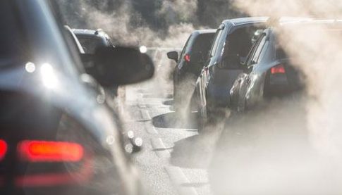 Line of cars in heavy traffic on a smoky, exhaust-filled road in daytime.