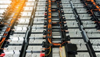 Row of silver battery modules in a rack with orange cables and black connectors in a power storage array