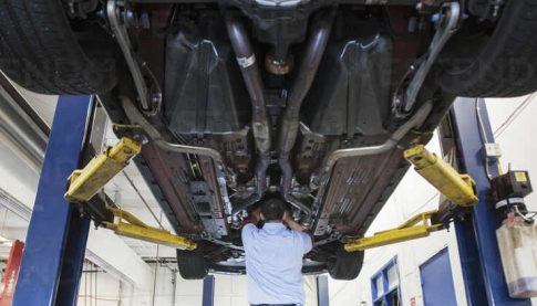 Mechanic working underneath a car lifted on a hydraulic hoist in an auto shop.